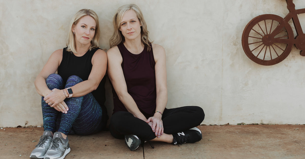 alt="sarah and missy wearing athletic apparel sitting next to bicycle"